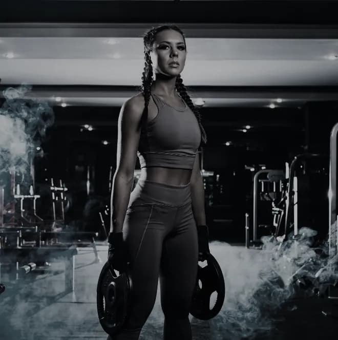 A lifter standing square to the camera with a weight plate in each hand, lit through smoke